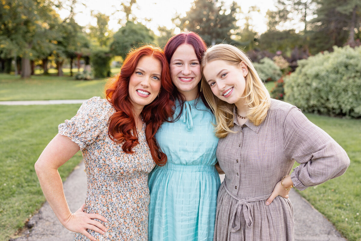 A mother with her two daughters standing close together, sharing a joyful moment in a picturesque outdoor setting.