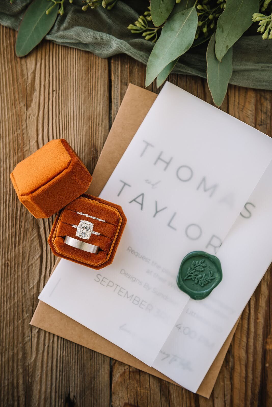 Rust orange and emerald green details for a wedding day including rings and invitation.