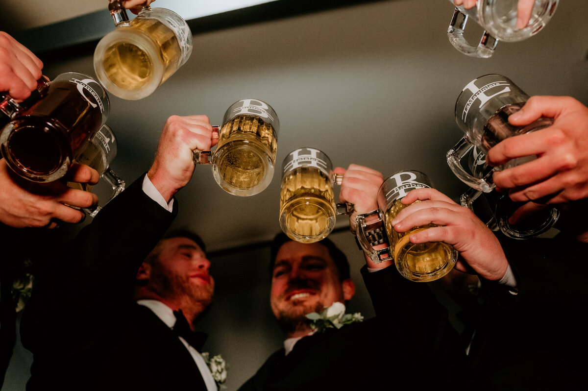 groomsmen holding their glasses of beer and toasting to the wedding