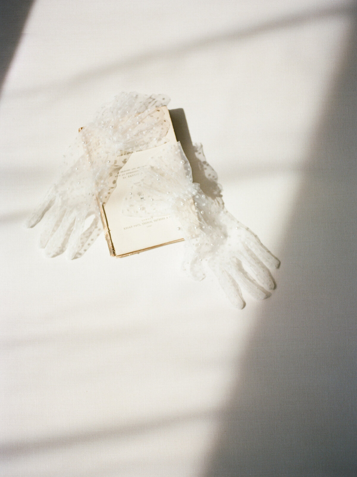 ethereal flat lay, directional light, pearl-studded tulle gloves, antique book