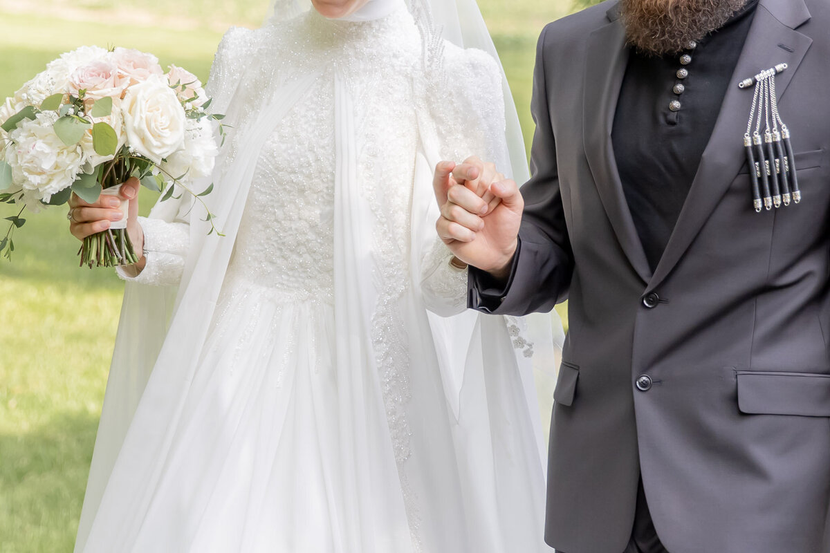 A close up of a bride and groom holding hands and walking. The photo is cropped so you can't see their faces.