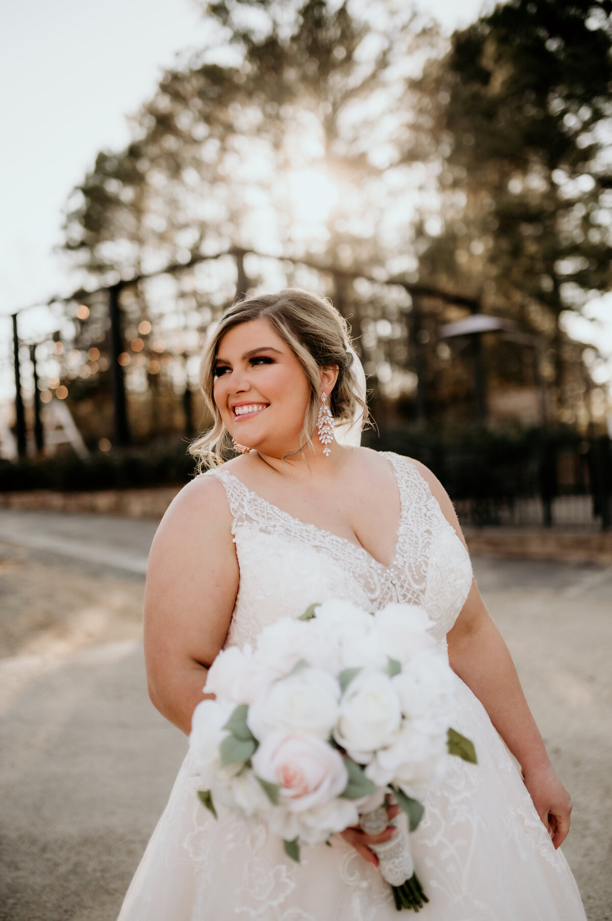 Little Rock wedding photographer photographs bride in a tulle and lace wedding dress with a white peony bridal bouquet as she smiles and stands in the woods
