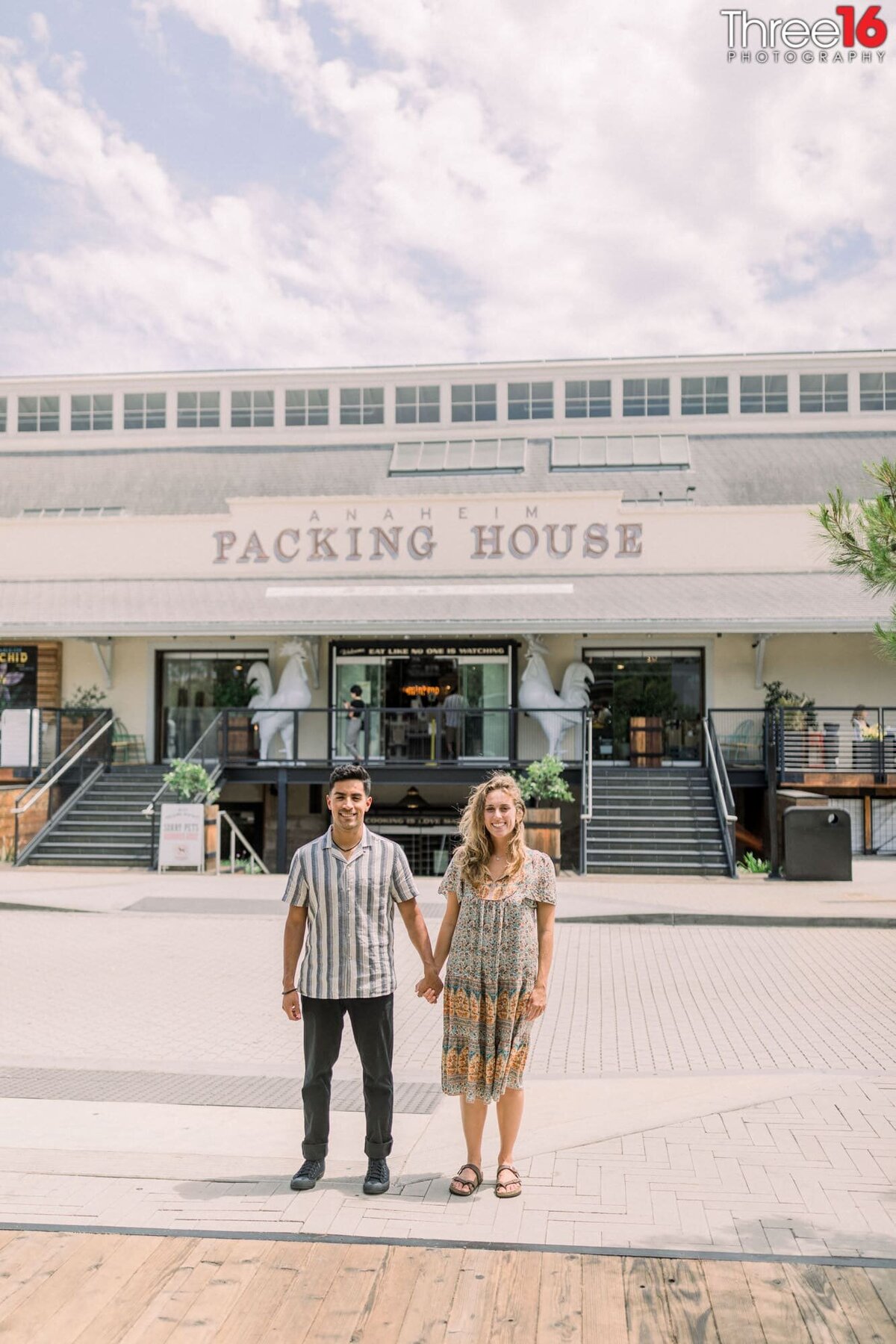 Engaged couple hold hands in front of the Anaheim Packing House