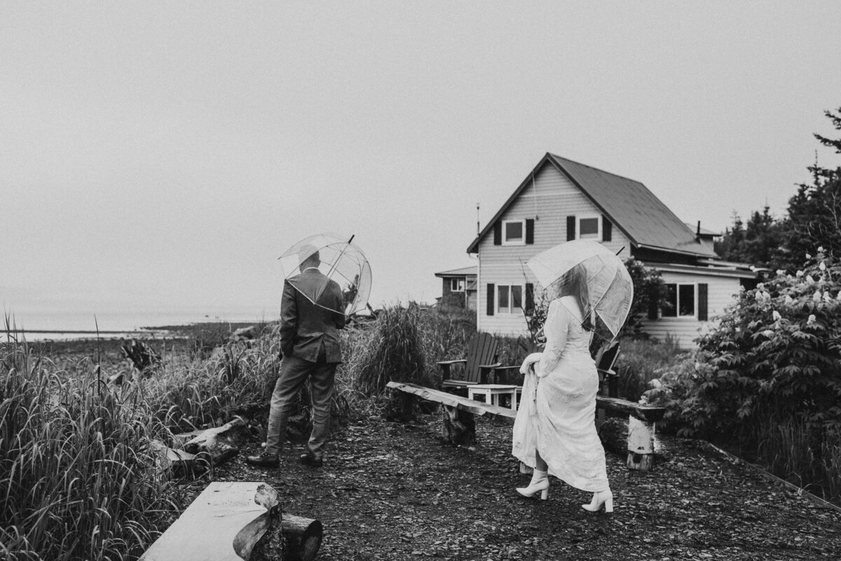a bride walking up to a groom on their elopement day about to share in a first look, standing on a foggy beach with an old cabin behind them