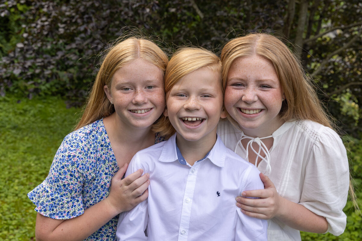 Søskenfoto  nærbilde av tre søsken som smiler og ler sammen. De har hodene tett sammen og ler mot kamera.