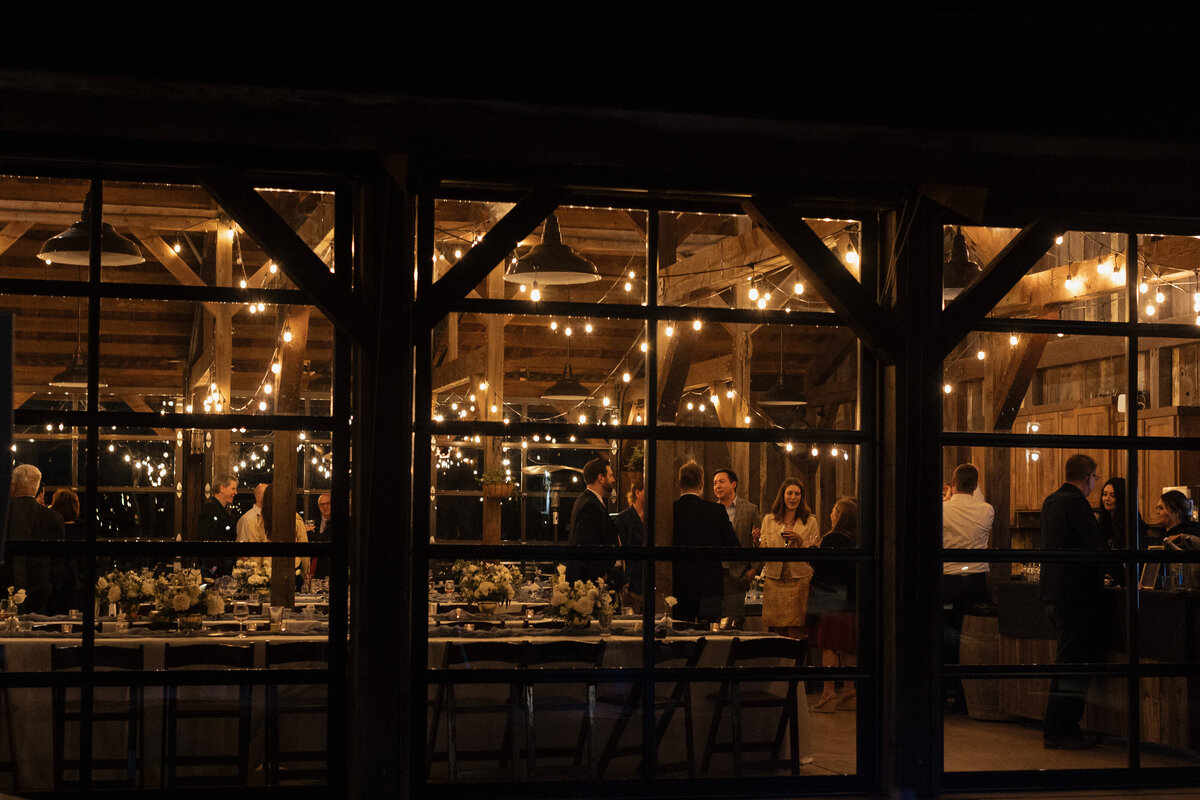 Guests enjoy a warmly lit barn reception, with string lights creating a cozy and elegant ambiance.
