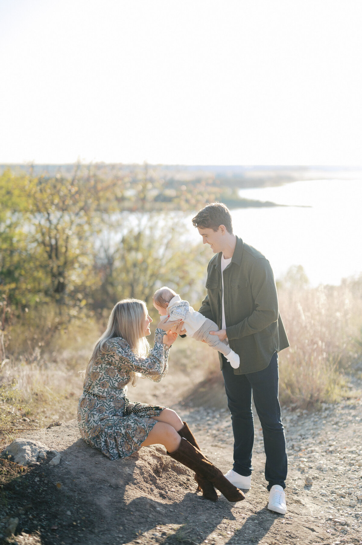 parents hold baby boy between them with lake in the backdrop fort worth family photography