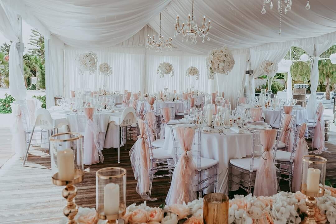 Banqueting tables decorated with peach tones sit under a white marquee with open sides