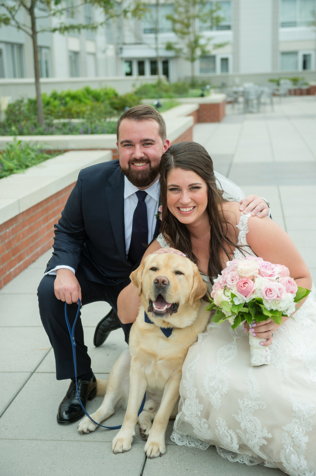 Bride and groom with a golden retriever wearing a bowtie.