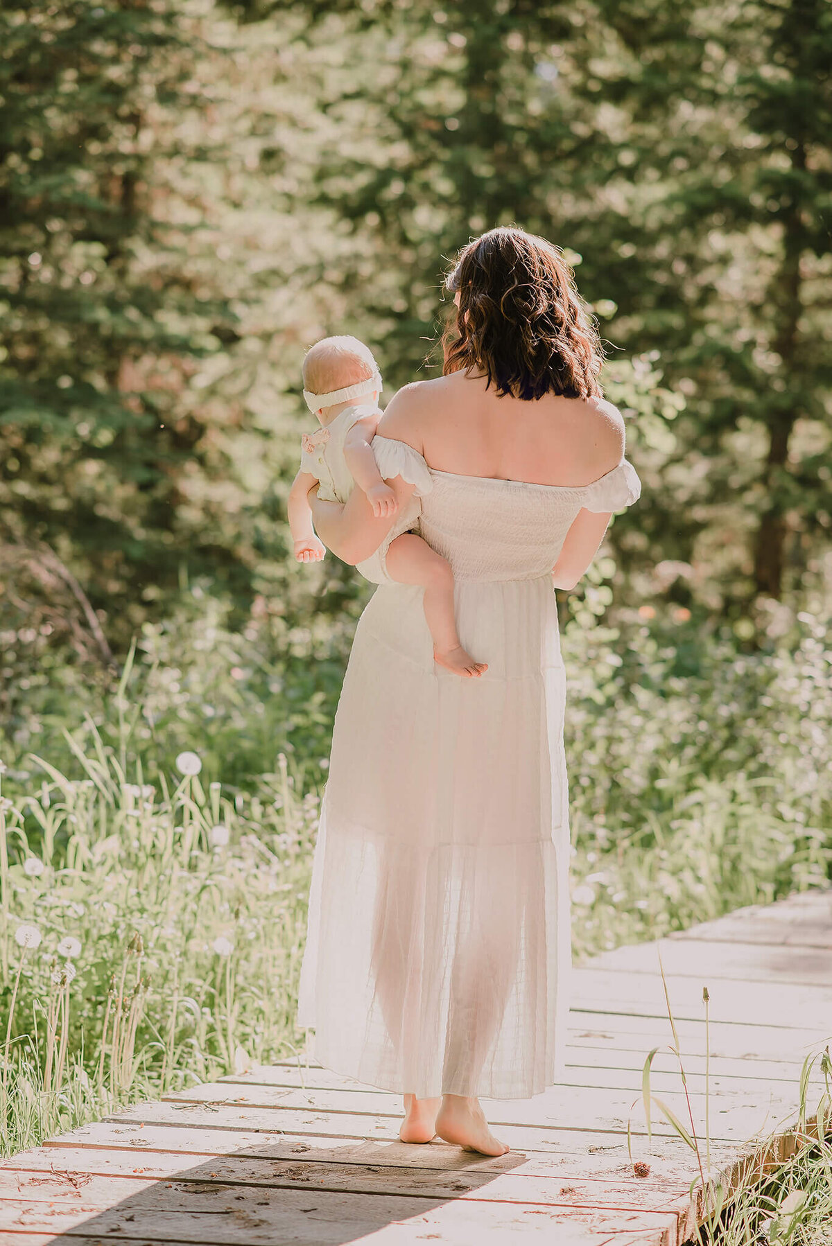 A mother and daughter walk away from the camera facing a backlit beautiful sun in the forest.  Captured by Brittany Danielle