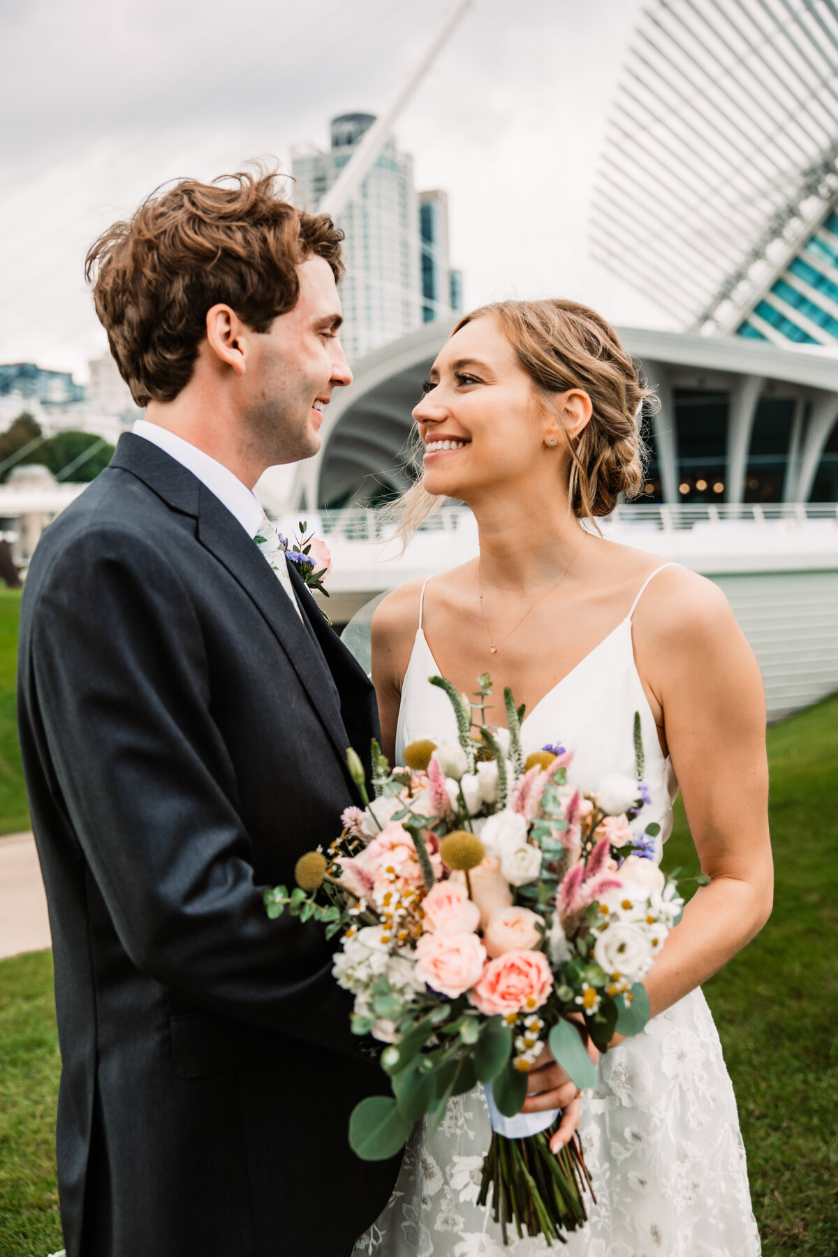 A bride and groom smile at each other while embracing in the lawn of their wedding venue