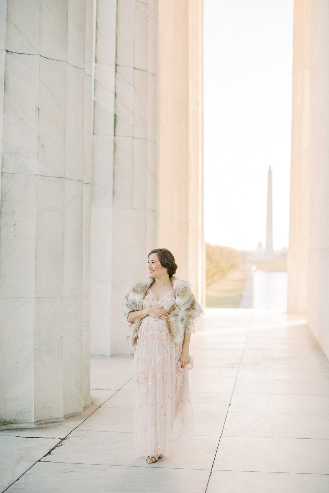 Pregnant mother in pink Needle & Thread sequin dress walks along the columns in the Lincoln Memorial.