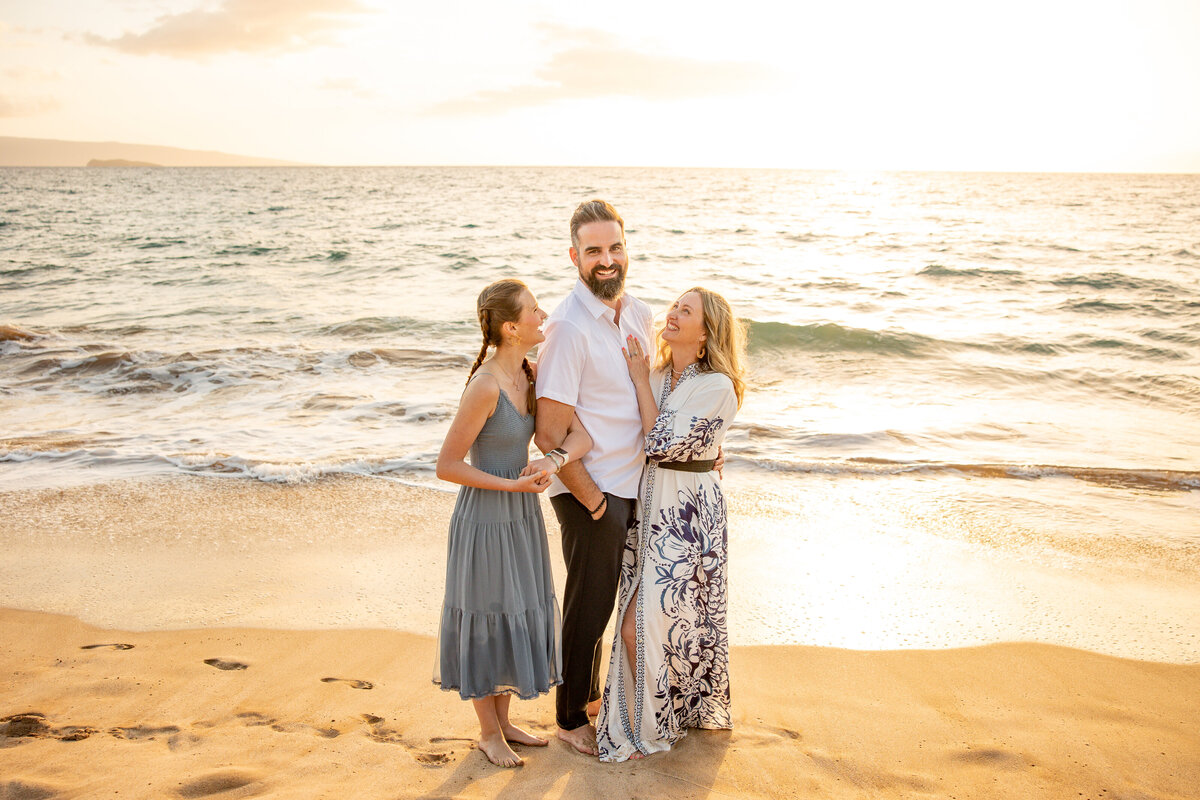 Maui Family Photographers capture woman laughing at husband while daughter looks up at them during family beach photos in Maui