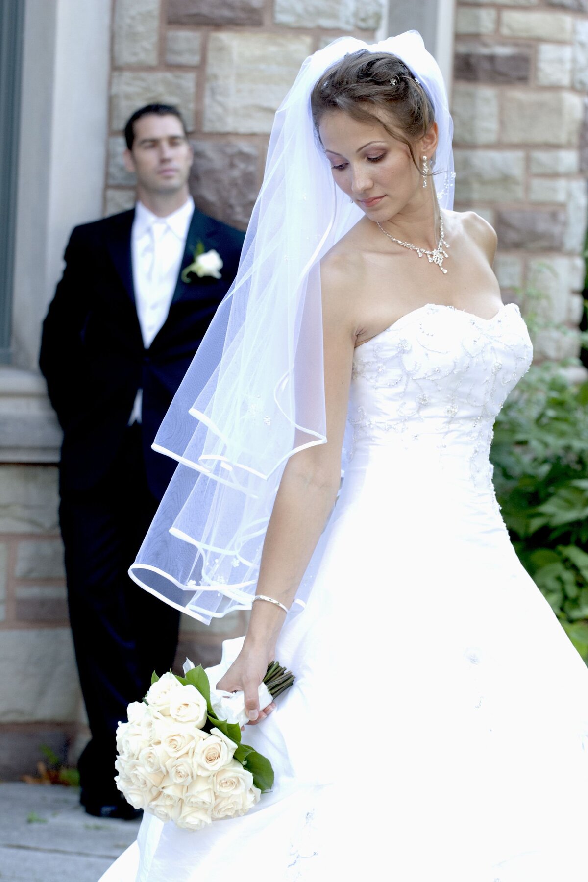 The bride, in a graceful stride, holds her bouquet close while looking back over her shoulder at the groom. This candid shot captures a moment of affection and anticipation as the couple enjoys their special day.