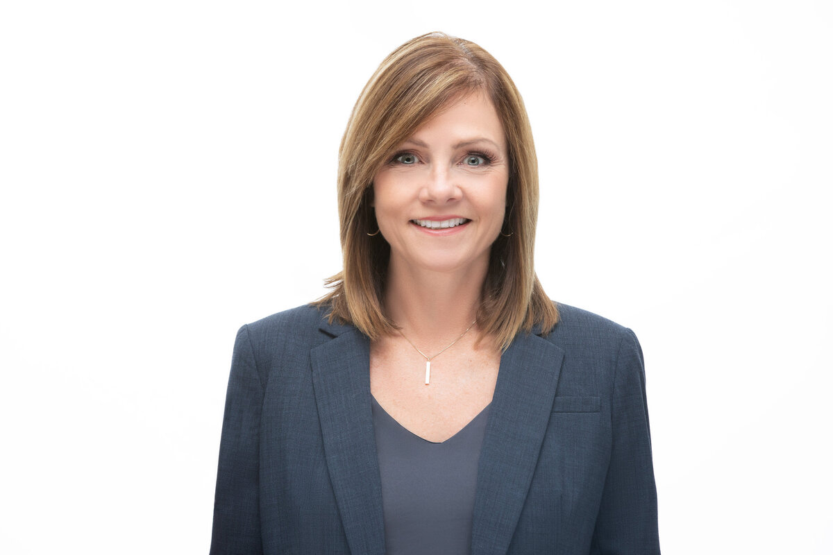 An executive woman with shoulder length brown read hair wearing a grey blazer poses for a professional headshot on a white background for Janel Lee Photography studios Cincinnati Ohio