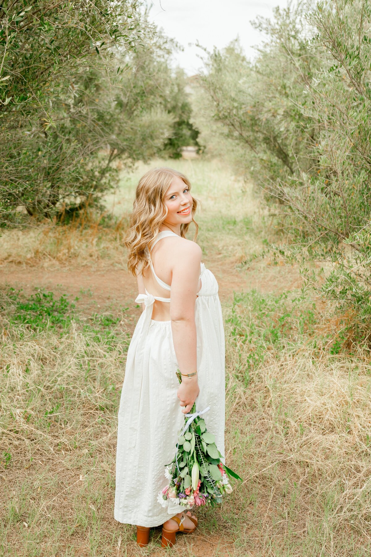 senior girl holding flowers in the field smiling at camera 