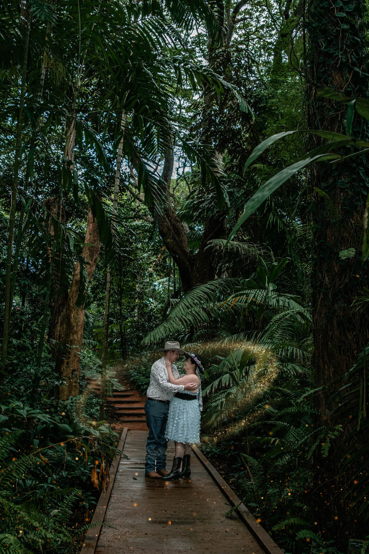 A couple embraces in a lush rainforest, surrounded by vibrant greenery and dappled sunlight filtering through the leaves - photo by Jamie Simmons
