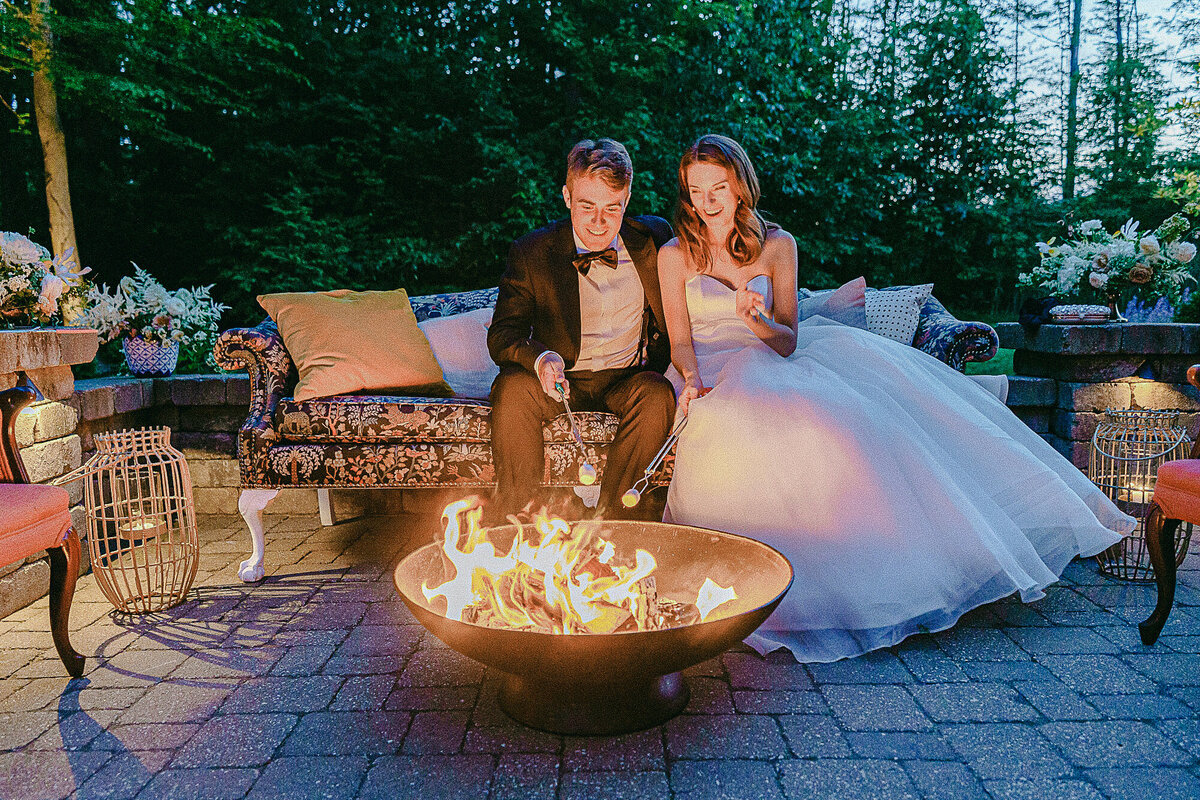 Bride and Groom roasting marshmallows at the patio fire pit at their intimate tented estate wedding reception