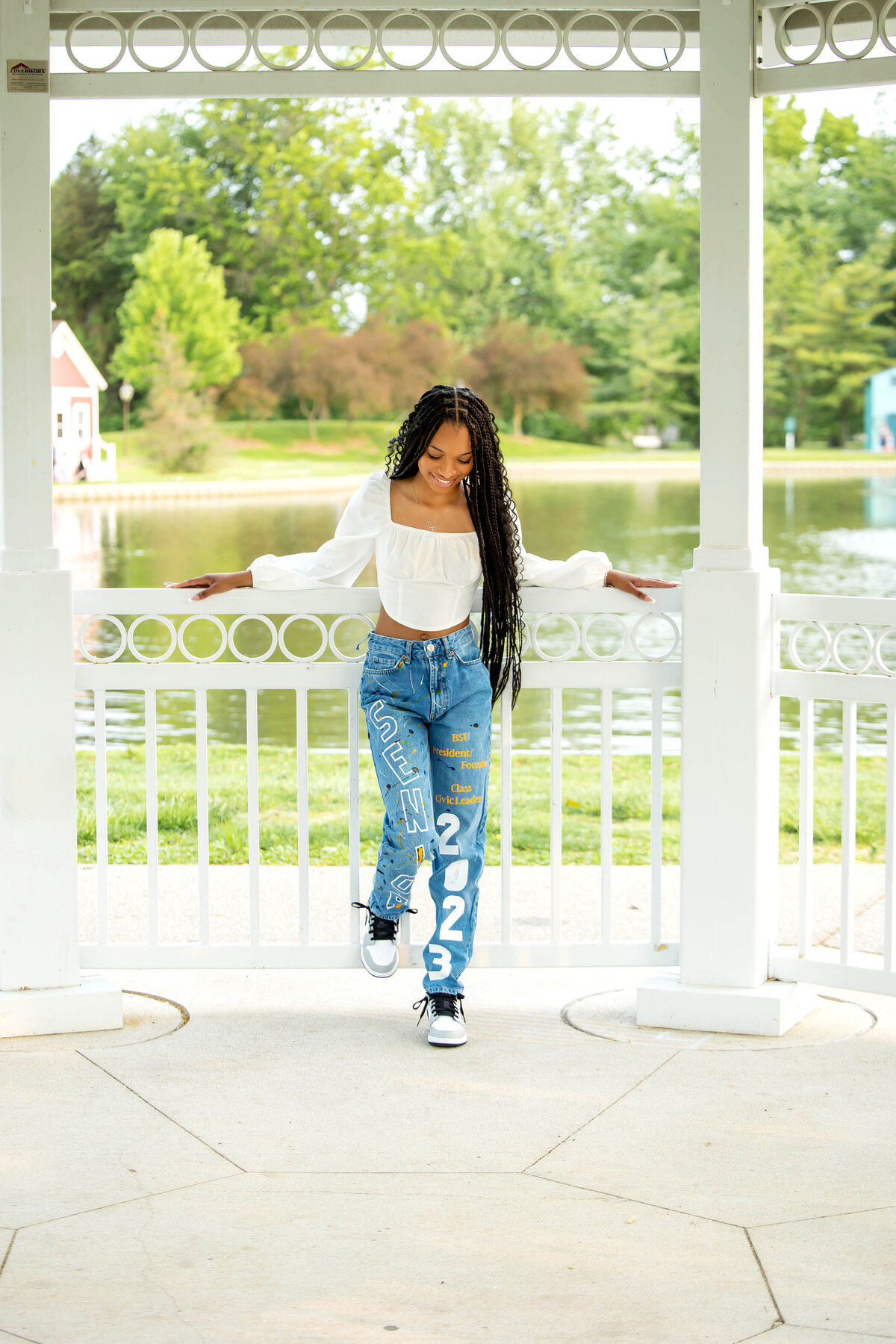 Taylor Heritage Park Photoshoot | Taylor Michigan Senior Photographer, African American senior girl wearing a white princess sleeve blouse, decoratded blue jeans, and gray and whie Nikes posing in a gazebo