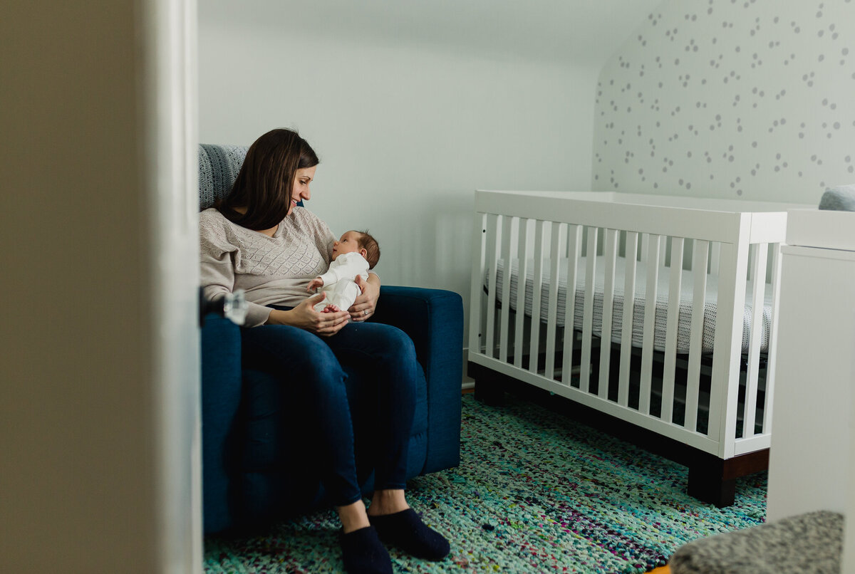 Mom holding newborn baby sitting in chair.