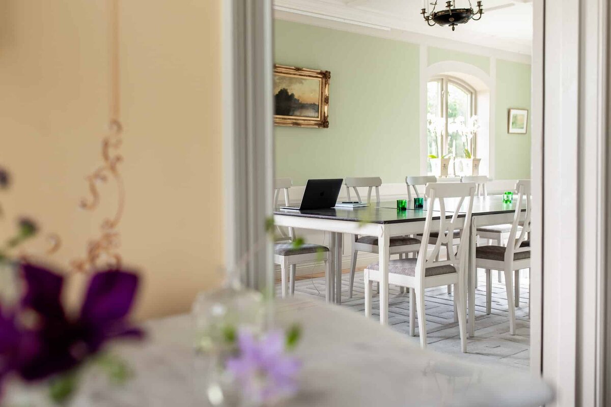 Ljus konferenssal med lantlig inredning, gröna väggar och vita trästolar – perfekt för möten eller måltider på pensionat.