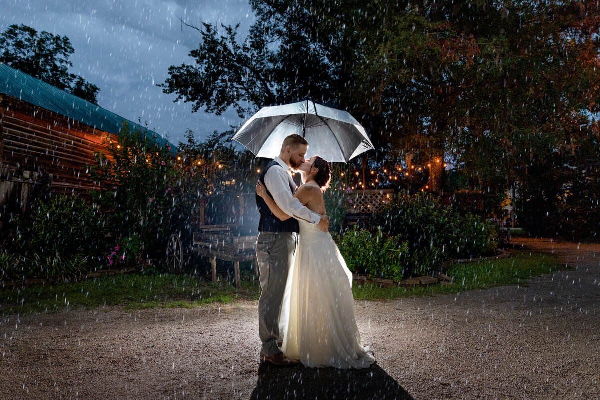 A bride and groom embrace under an umbrella on a rainy wedding day