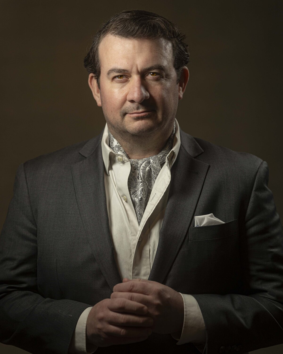 Business headshot in MA of man in gray suit and tie, seated with hands folded, photographed by Rob Faber Photography.