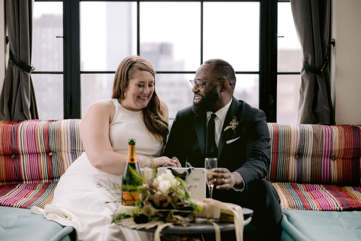 The bride and the groom are happily drinking champagne inside a Ludlow Hotel room in New York City.