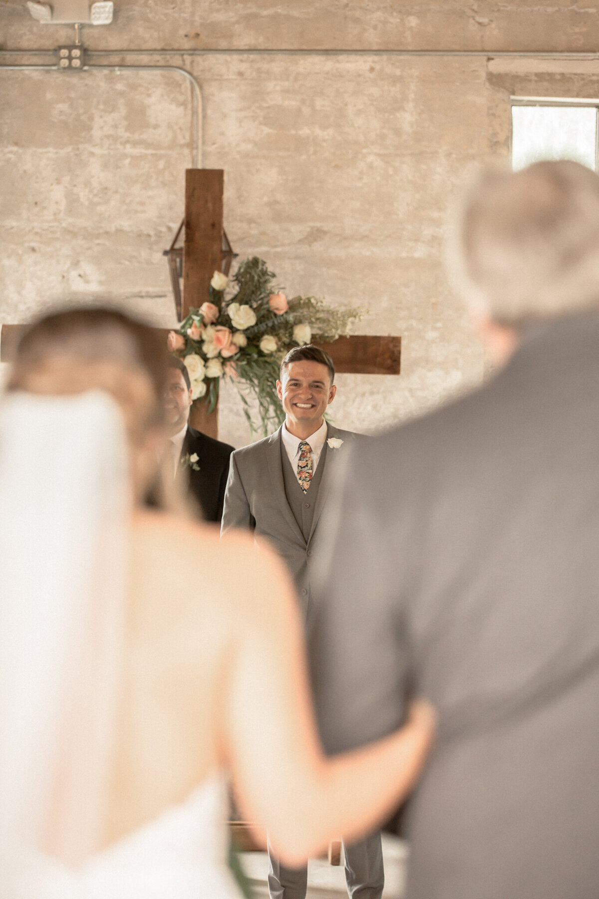 The groom, framed by his bride and her father, beams as she walks down the aisle toward him