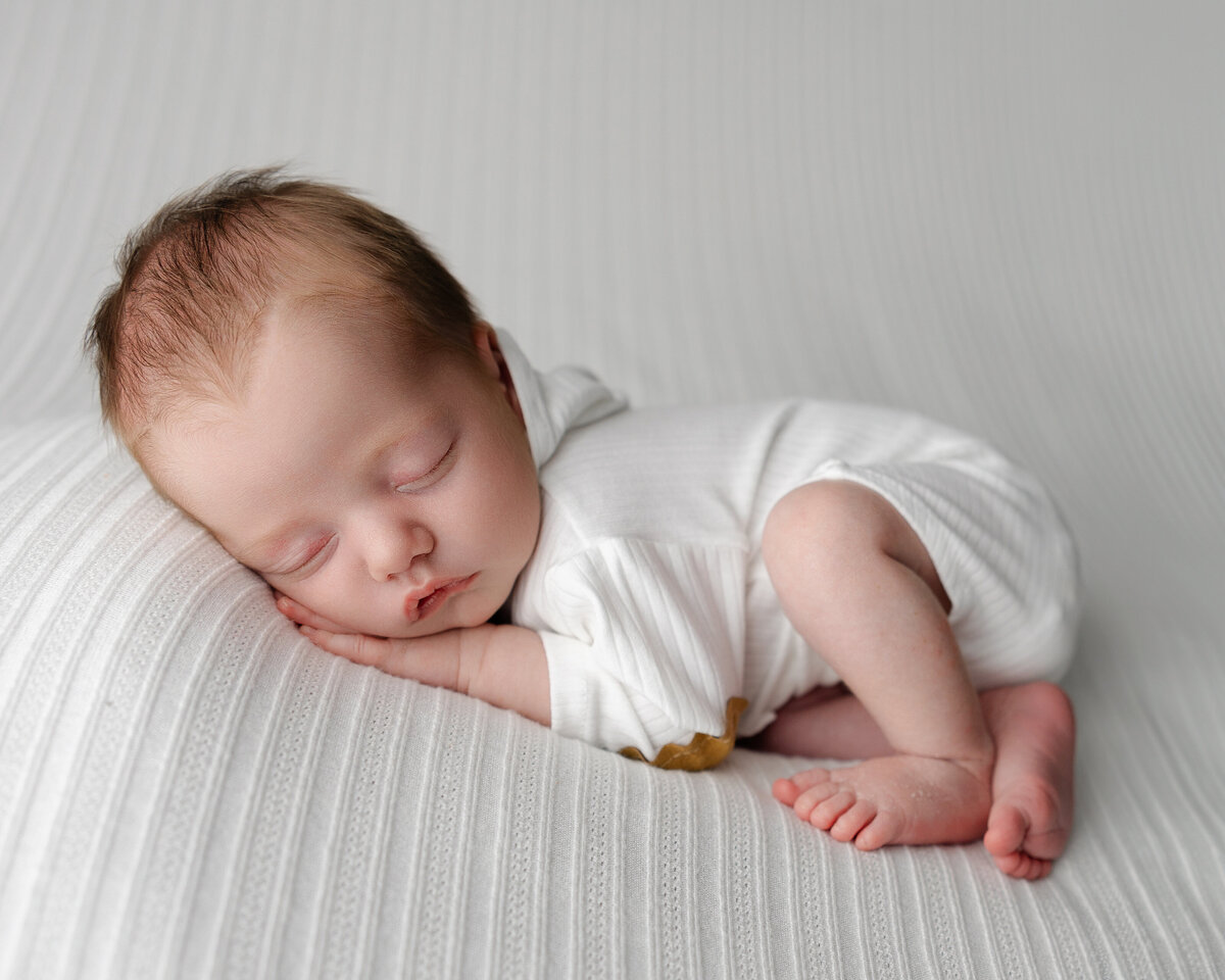 Studio newborn portrait featuring clean, natural tones with baby resting in a relaxed position, simple, timeless, and serene. Captured by Inland Empire newborn photographer Kaitlyn Dawn.