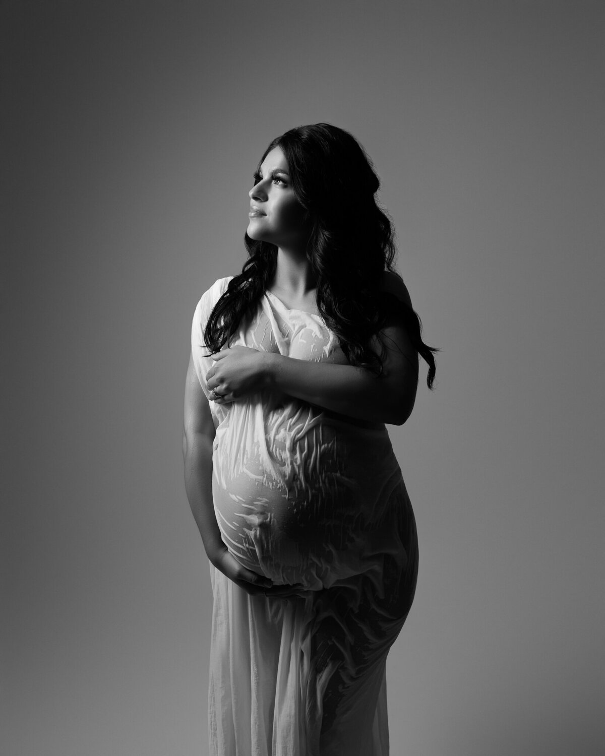 Artistic black and white maternity photo using sheer, wet-look fabric to contour the belly, photographed in studio in Austin.