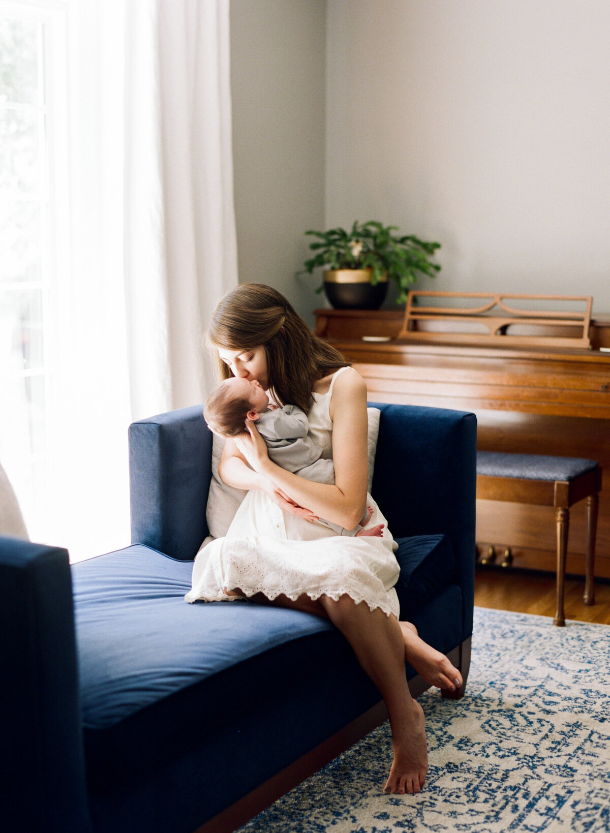 Mom holds her newly adopted son close and kisses him while sitting on a blue velvet couch. Image by Raleigh newborn photographer A.J. Dunlap Photography.