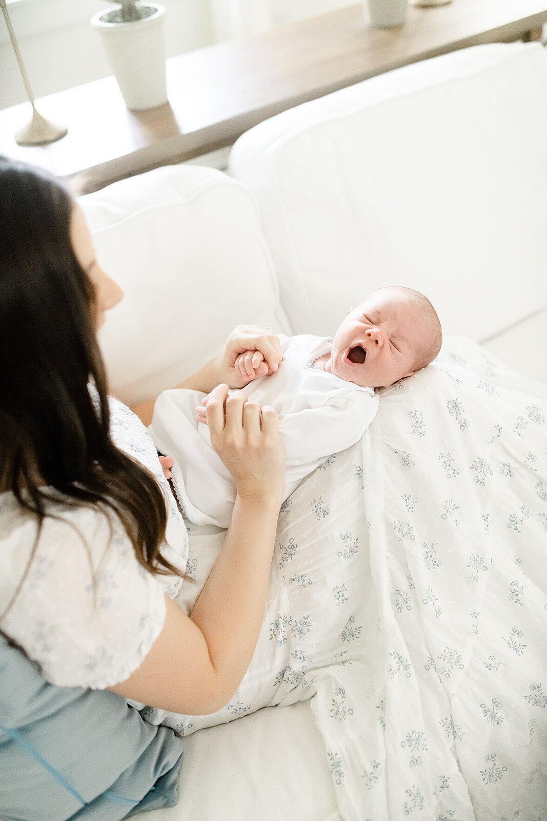 a newborn yawns in the lap of his mother on a white couch