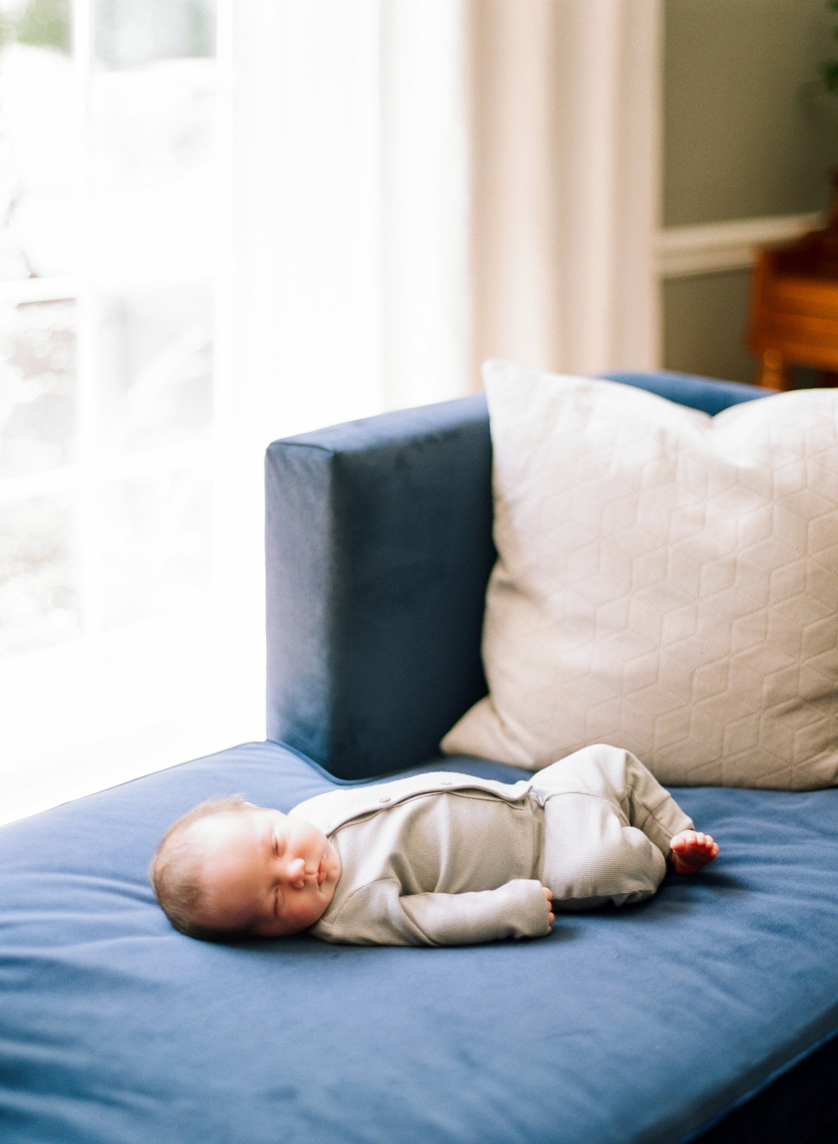 Baby lies on a blue couch fully relaxed and calm during a Raleigh newborn photography session. Photographed by Raleigh newborn photographers A.J. Dunlap Photography.