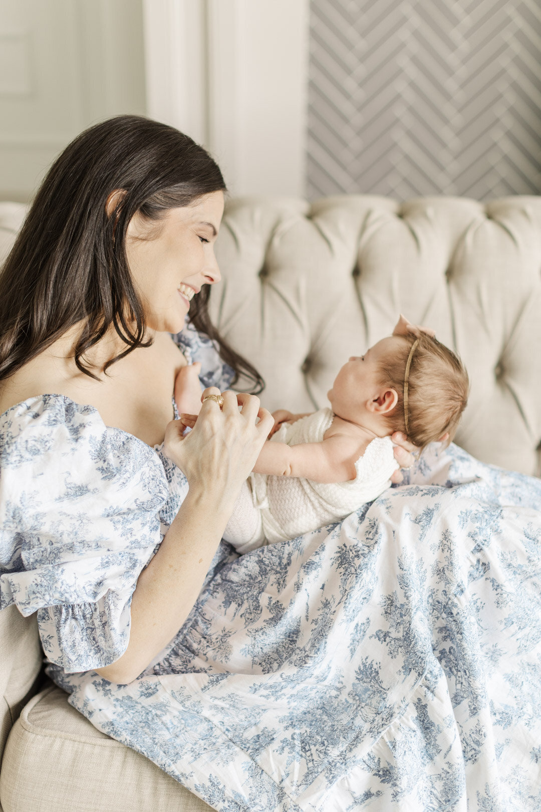 mom holds baby on lap wearing blue dress on a sofa for katy newborn photography session