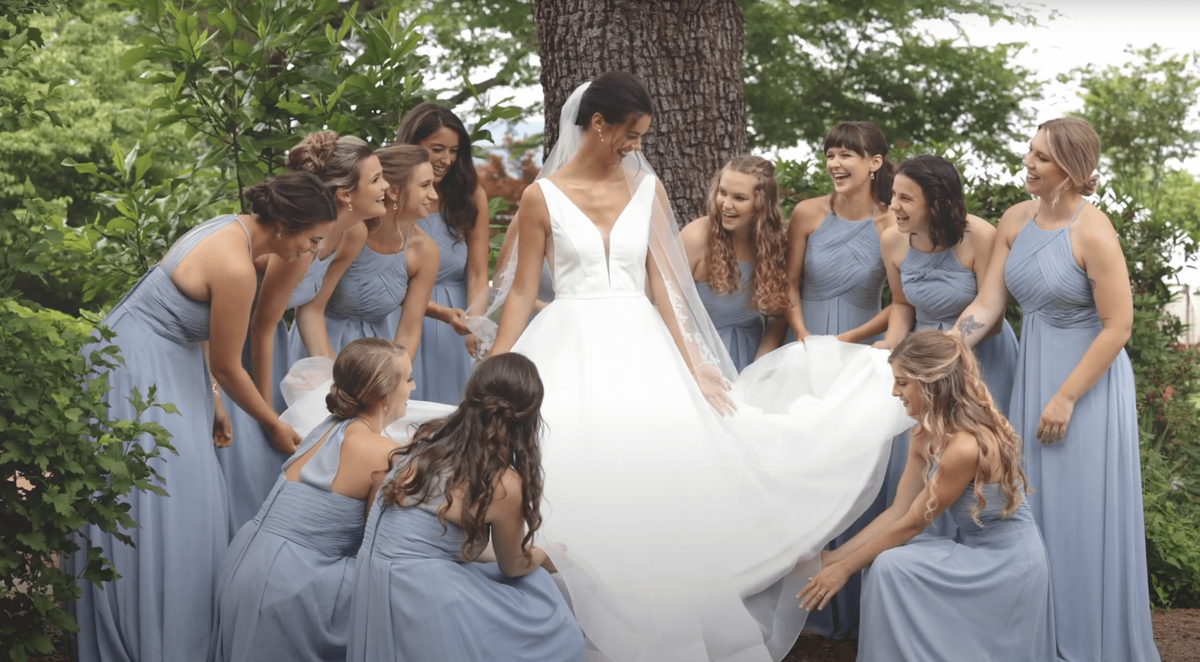 Bride stands in circle with bridesmaids in blue dresses