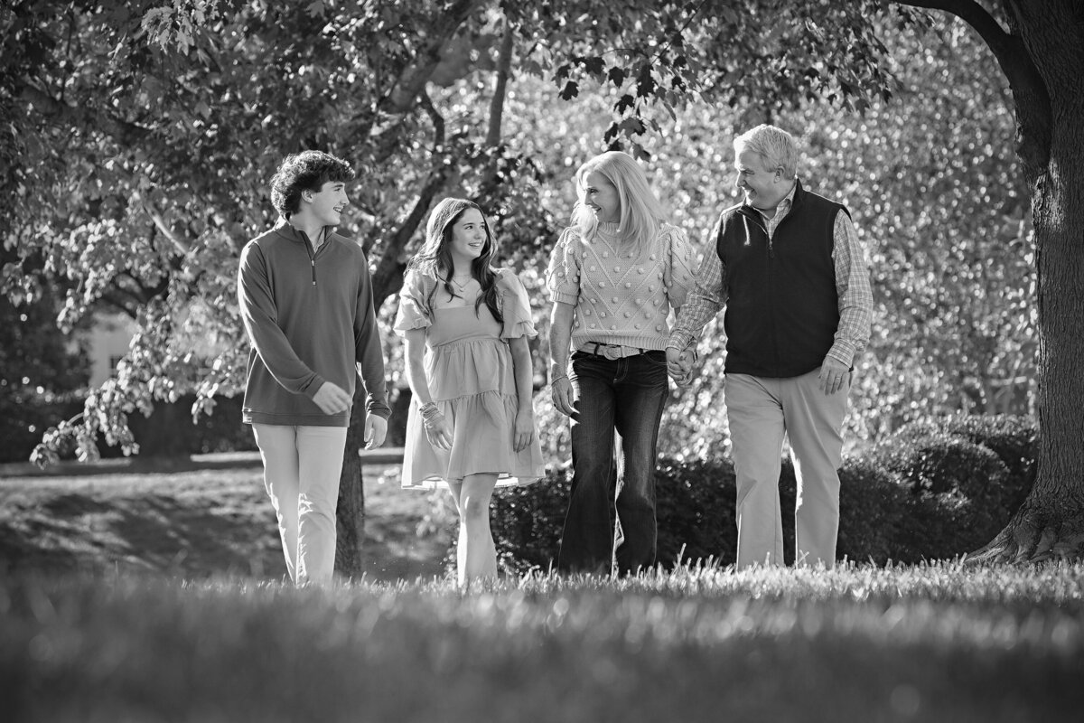 Black and white photograph of a family walking together along a tree‑lined path in Charlotte,  NC. 