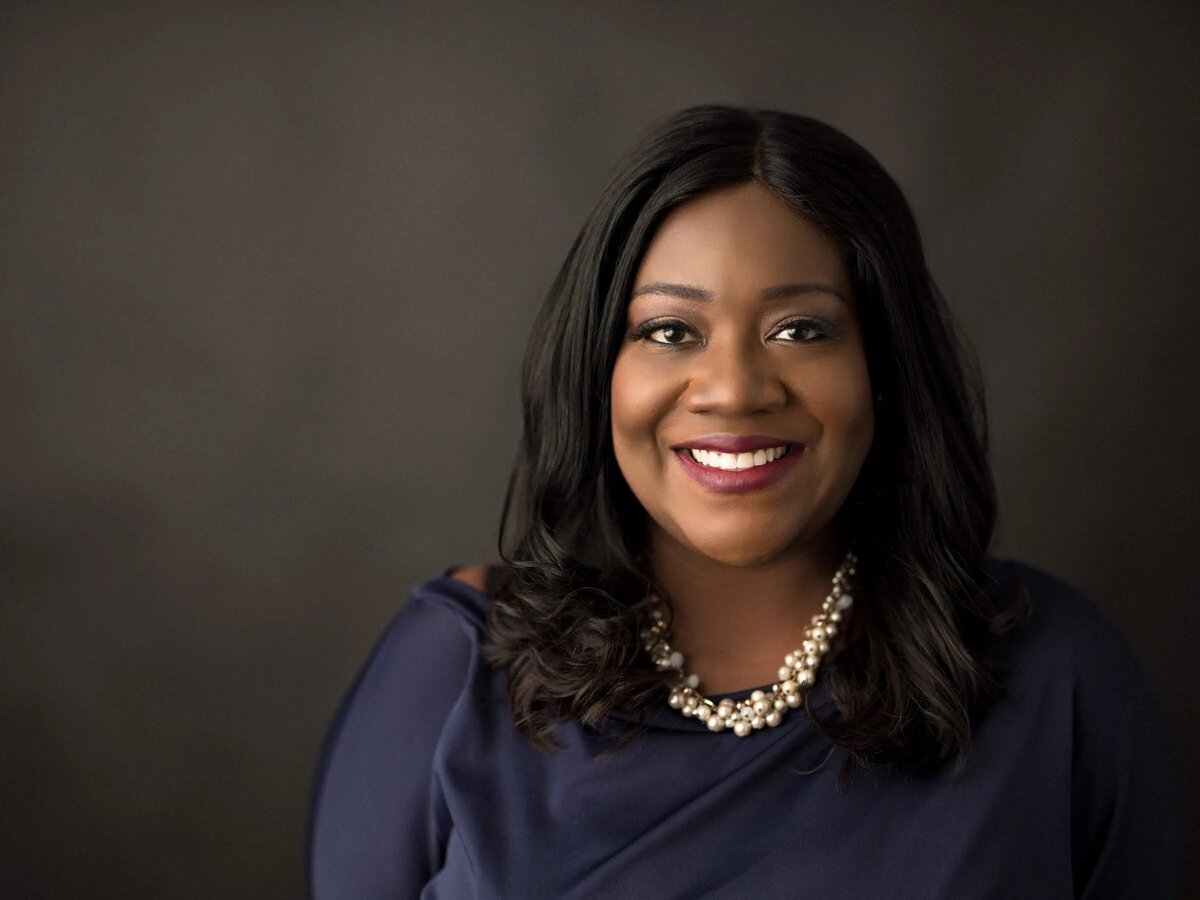 A woman smiling big in front of a black backdrop .