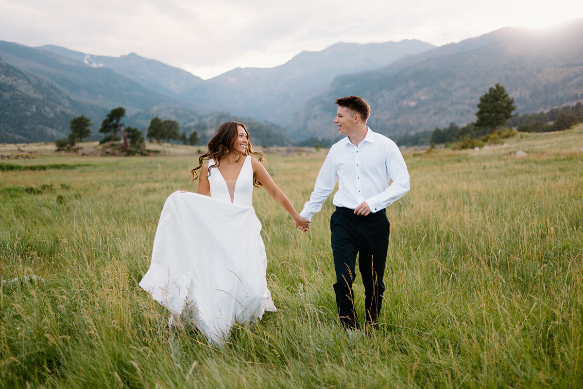 A bride and groom run hand in hand through a scenic Rocky Mountain National Park trail during their adventurous day after session.