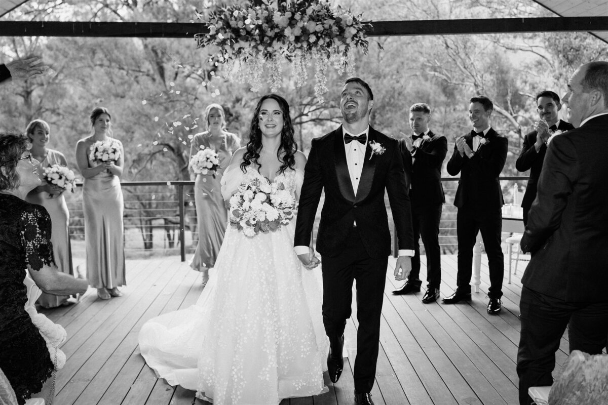 The bride and groom walk hand in hand, bathed in golden sunlight, as they exit the ceremony, their joyous smiles capturing the essence of their newfound union.