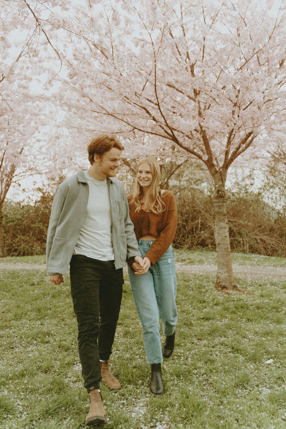 photo of guy and girl walking hand in hand in front of cherry blossom trees