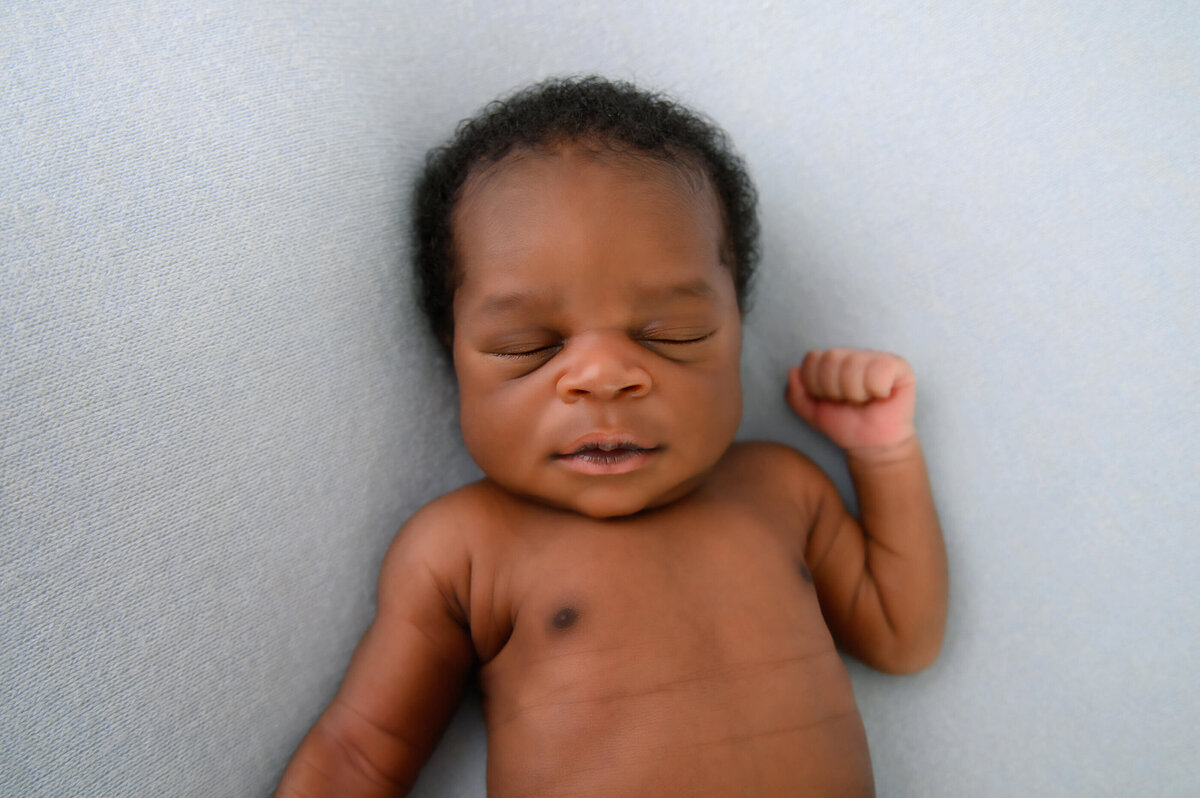 black newborn boy laying on a blue background for his newborn photos