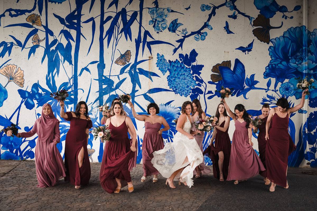 Bridesmaids wearing maroon dresses dance with the bride in front of a mural at Tom Ping Park in Chicago, Illinois
