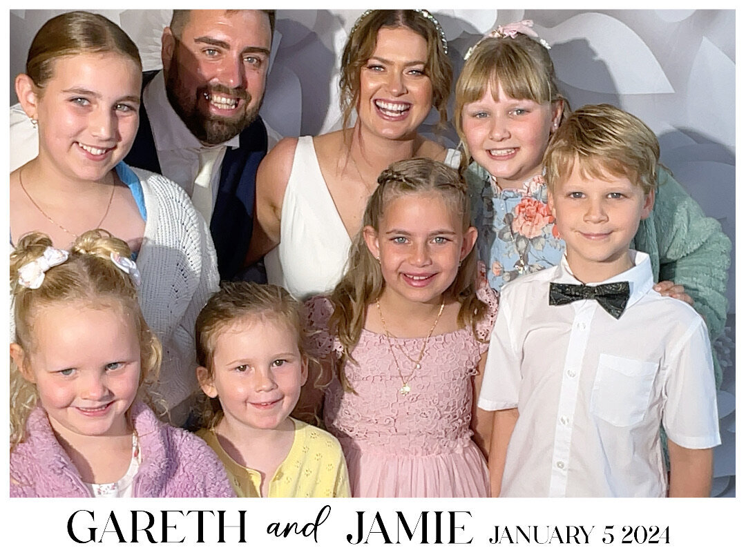 a bride and groom with six children pose in a photo booth