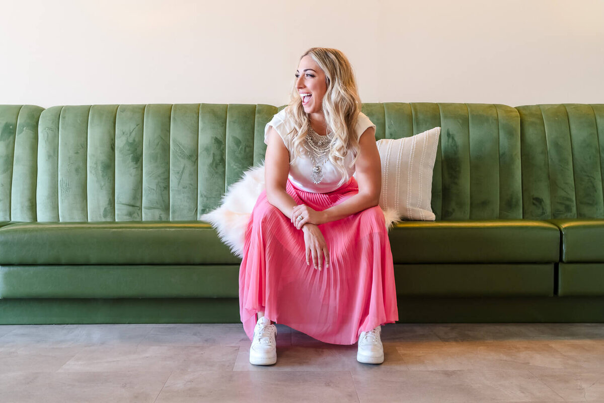 Anita, a local female entrepreneur laughing to her left while sitting on a green velvet couch in Just Peachy Kelowna.