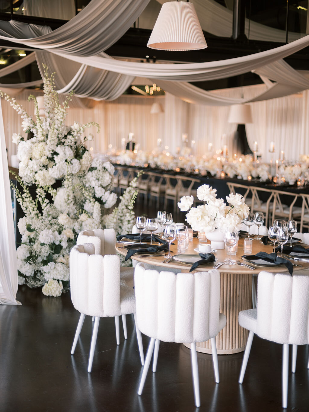 A beautifully decorated wedding reception with white florals, modern chairs, and a floral backdrop.