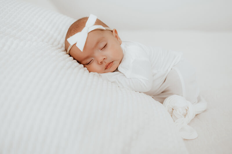 Newborn baby girl  sleeping on her belly while cuddled up on a white blanket.