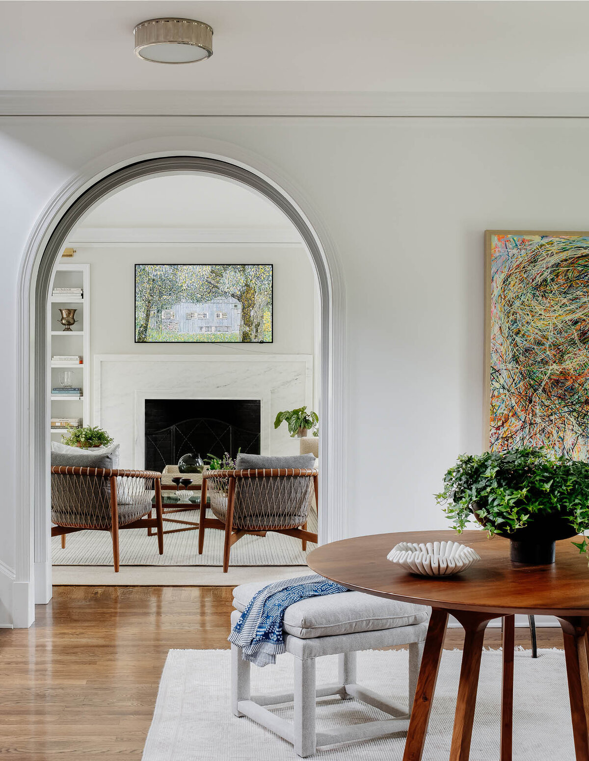 Step into a classic foyer in a Hingham farmhouse, where a mid-century walnut table pairs with modern benches, a neutral rug, and curated artwork displayed on walls with a gallery-like feel.