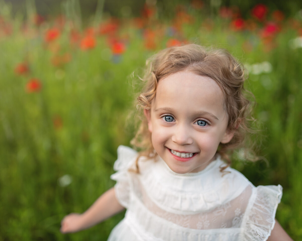 Joyful milestone portrait of a girl in white surrounded by blooming poppies—nature’s perfect frame for her glow.
