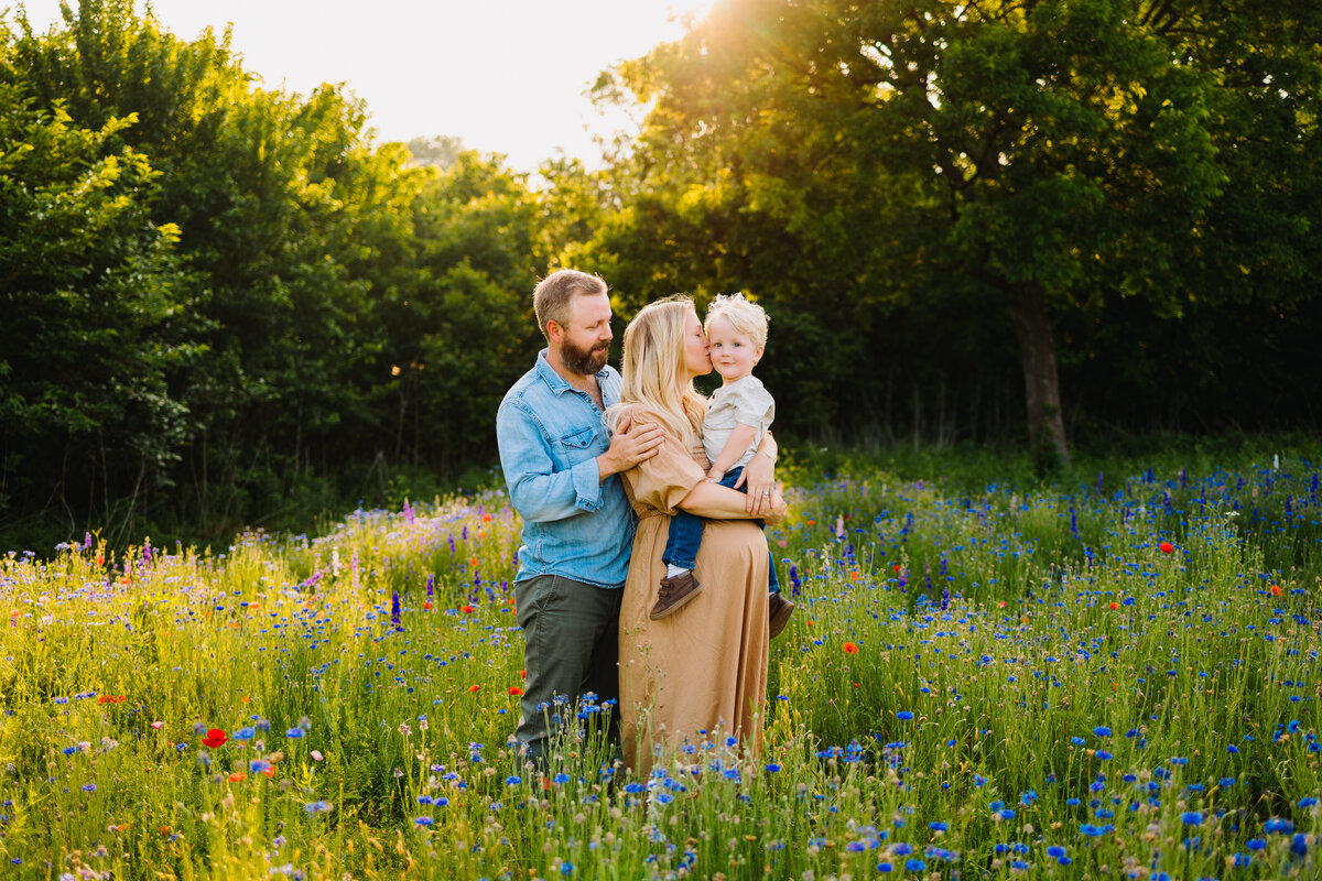 Family mini session photography with family. The woman is wearing a long dress and the man blue shirt. Behind them are trees with  flowers